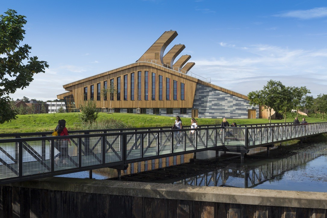 Students cross a bridge in front of the GSK Carbon Neutral Laboratory on the University of Nottingham campus