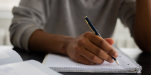 A man holds a pen over a notebook