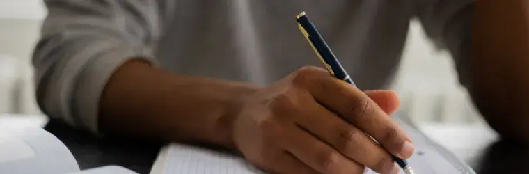 A man holds a pen over a notebook